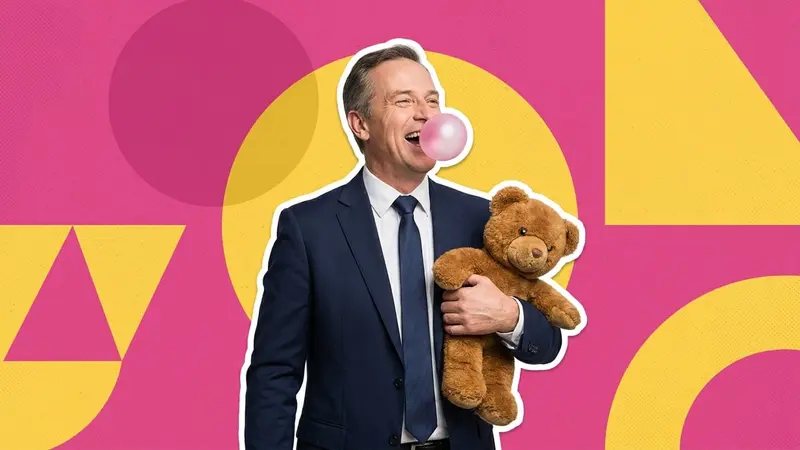 A man in a suit blowing a bubble-gum bubble and holding a teddy bear