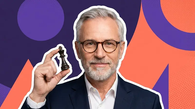 A silver-haired man in a suit with a calm smile holding a chess piece